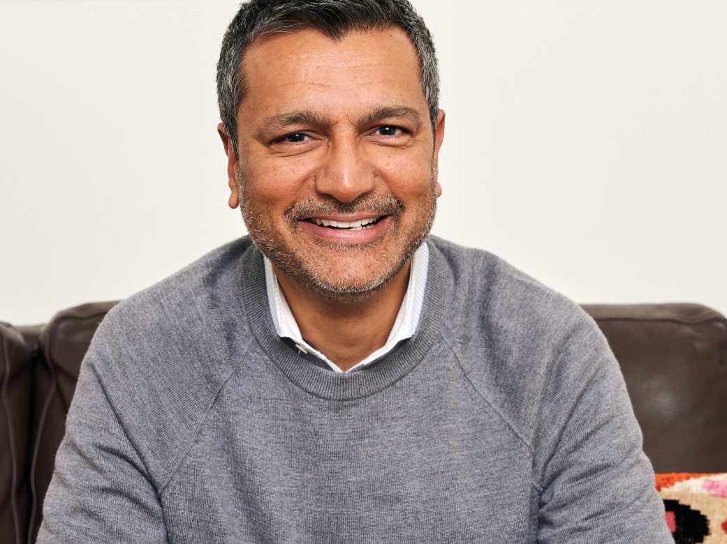 Dharam Rai, SVP of Customer Success at Sonos, sitting on a couch smiling