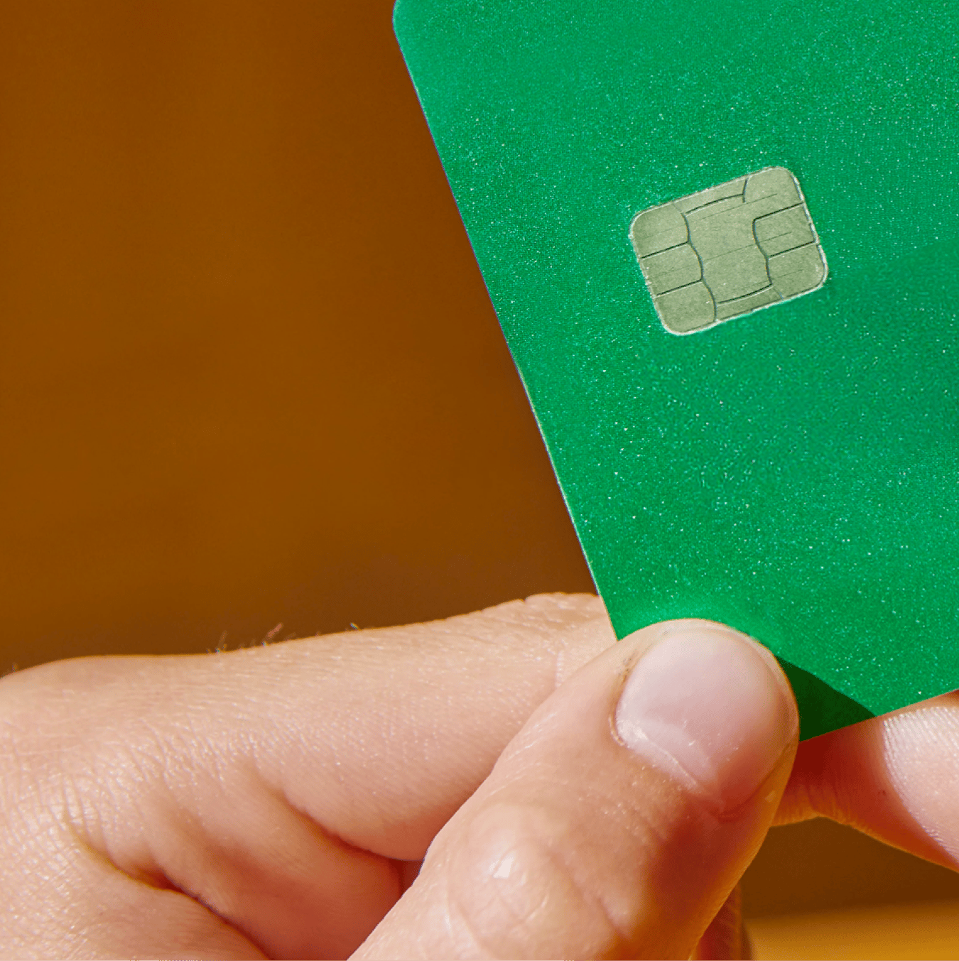 A hand holding a green card with a visible metallic chip.