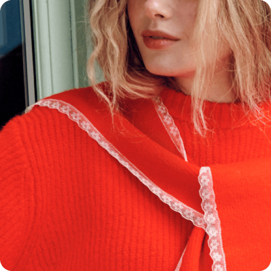 Close-up of a woman in an orange ribbed sweater with a matching scarf trimmed in white lace.
