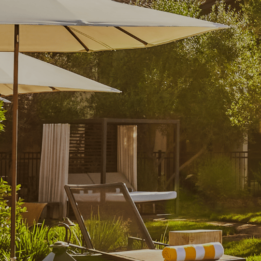 Patio umbrellas and a cabana with a lounge chair at a sunny hotel.