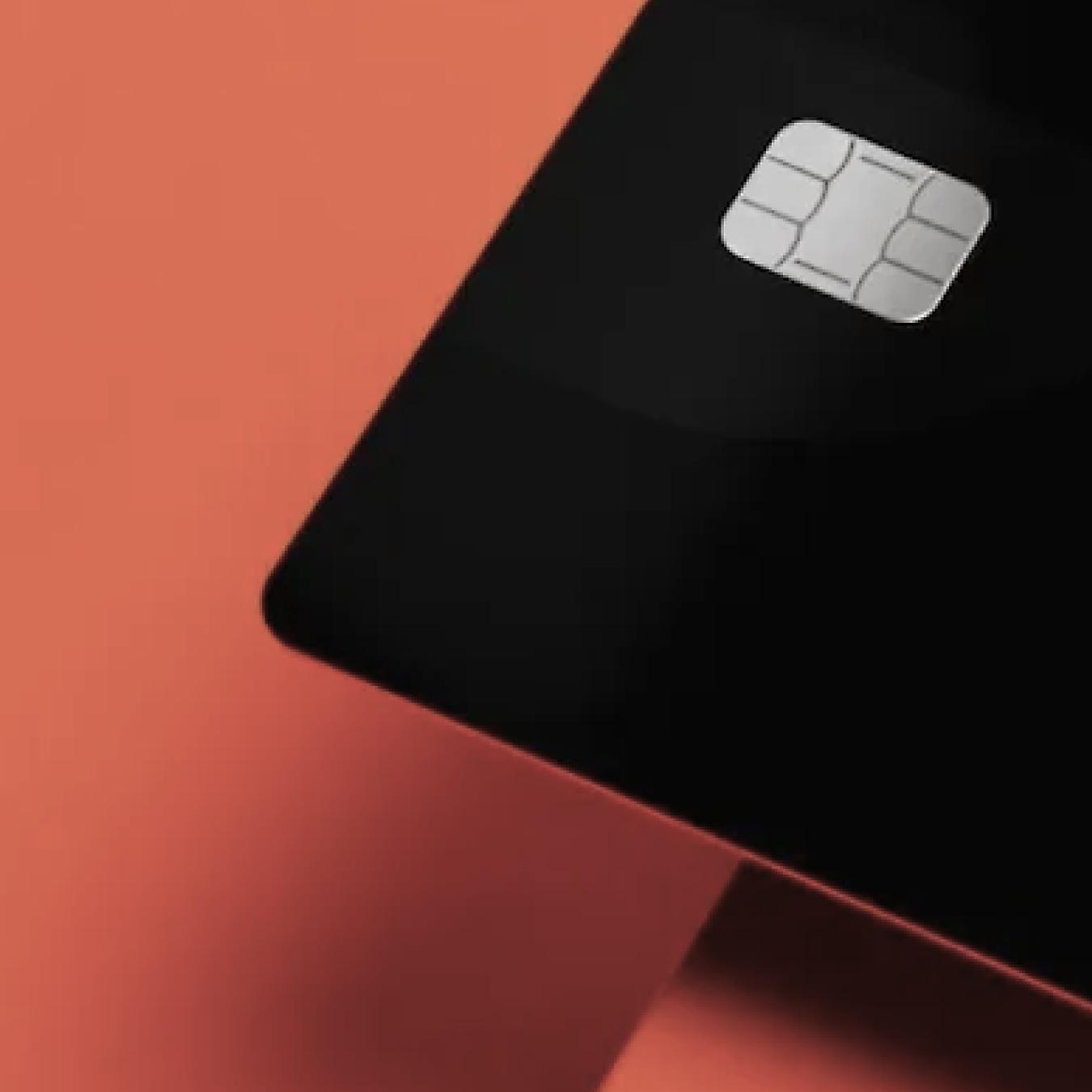 A black credit card with a silver chip on a coral background.