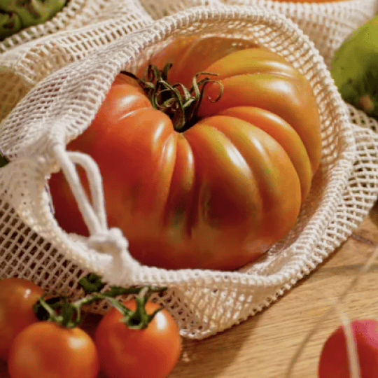 A large, red, ribbed tomato inside a white mesh produce bag.