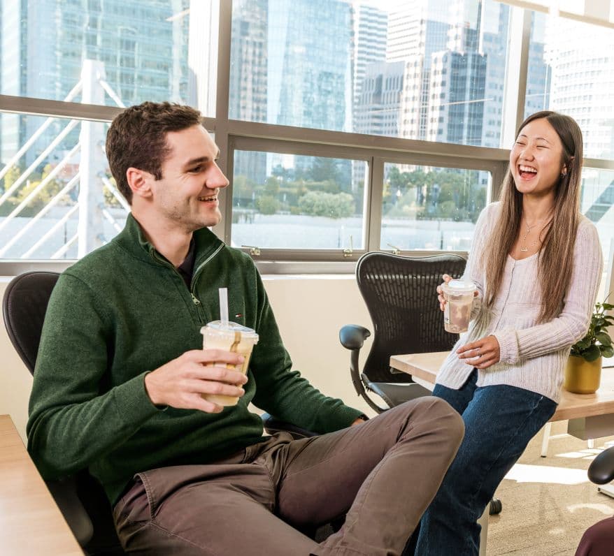 a man and woman laughing in coworking space while holding boba drinks