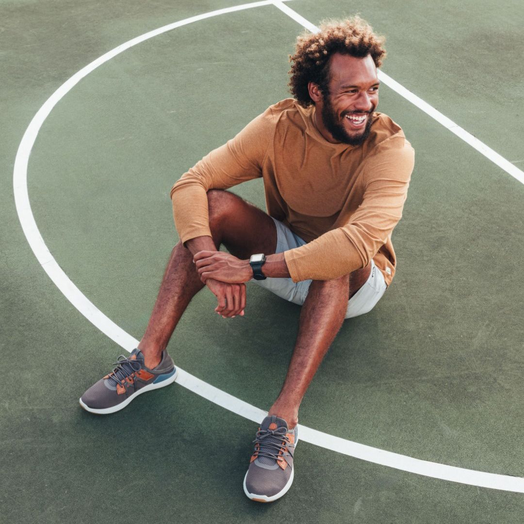 Man sitting on a basketball court, wearing OluKai shoes