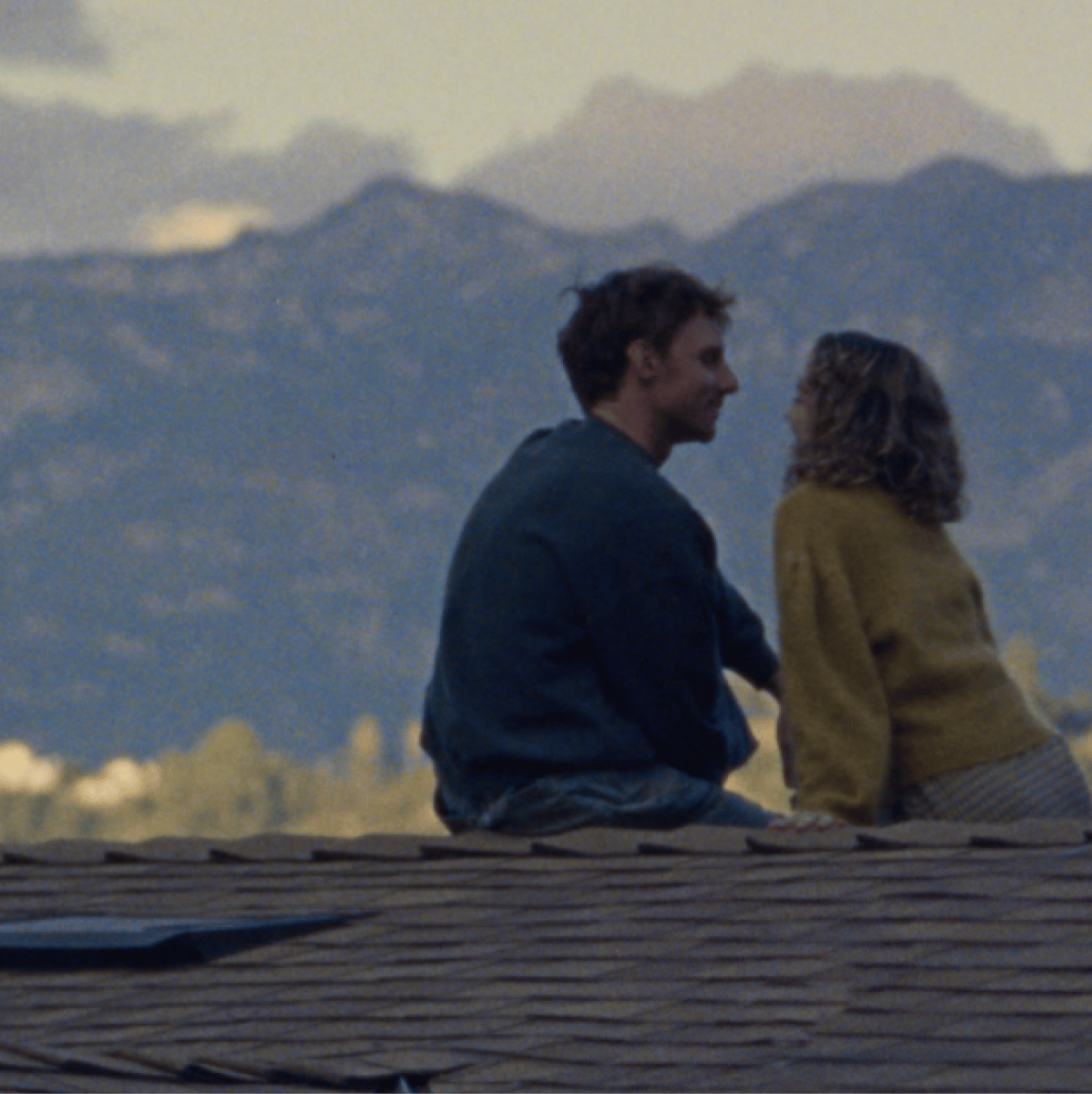 Couple sitting on a rooftop, gazing at each other with mountains in the distance.