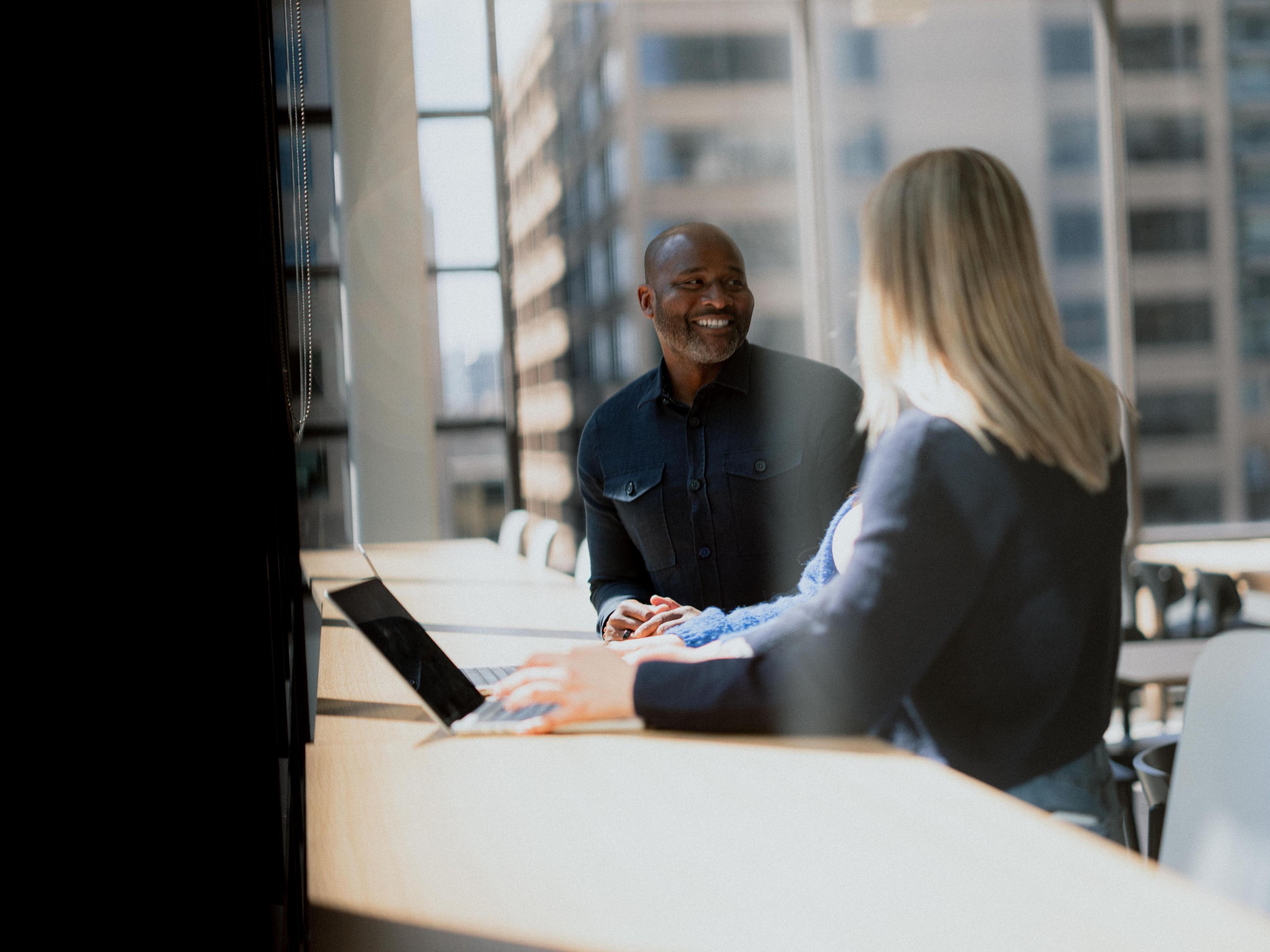 A meeting of three people, sitting at a table with two open laptops