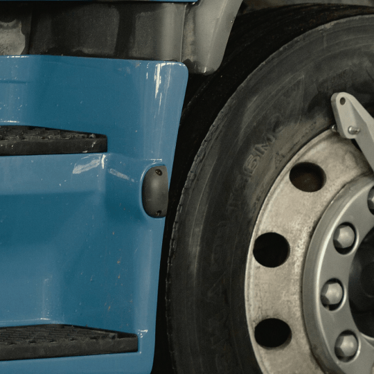 Close-up of a blue truck's side with a black step, small marker light, and tire.