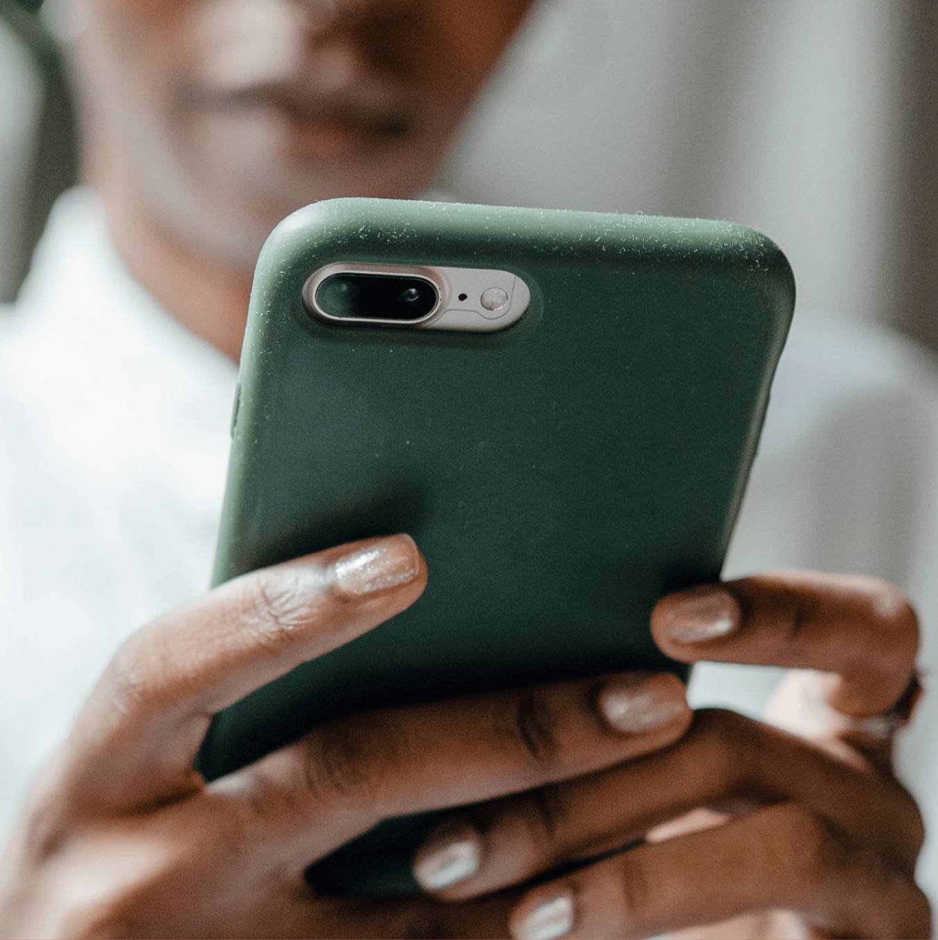 A person holds a smartphone with a dark green case, showing their hands with light nail polish.