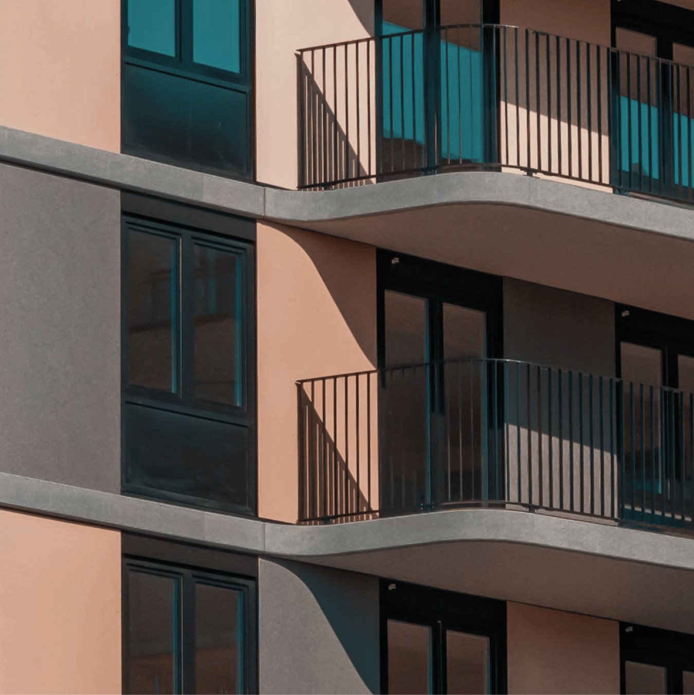 Modern building facade with alternating light beige and gray sections, dark windows, and curved balconies with black railings.