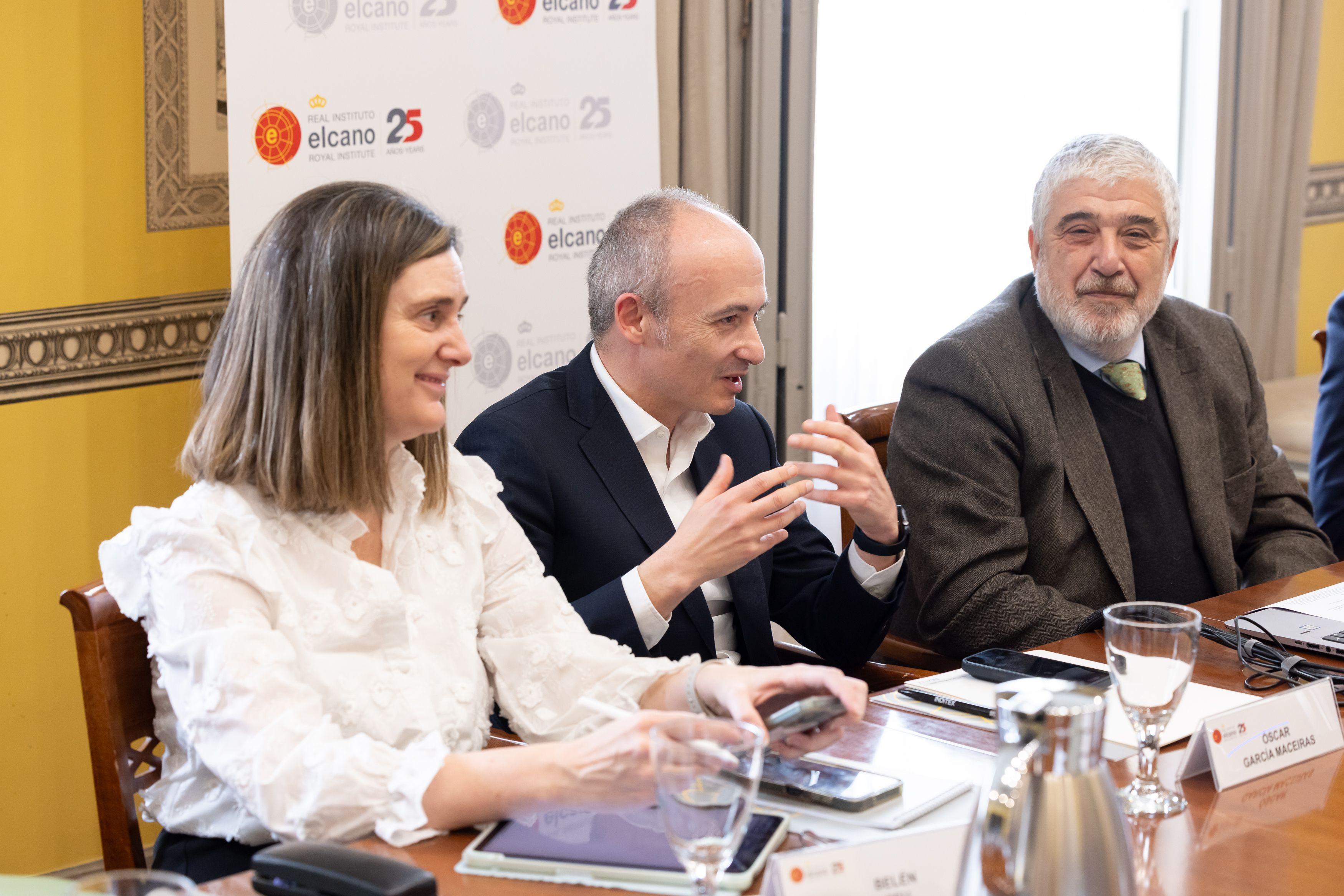 Three people at a meeting table, including a man speaking with hand gestures, and an Elcano 25 logo in the background.