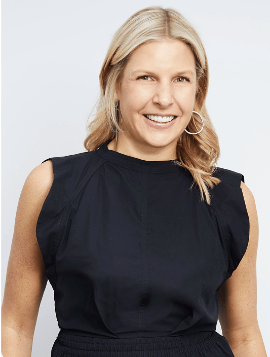 A smiling woman with blonde hair and silver hoop earrings wears a black sleeveless top.