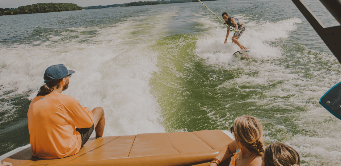A man wakesurfing behind a boat, watched by three women.
