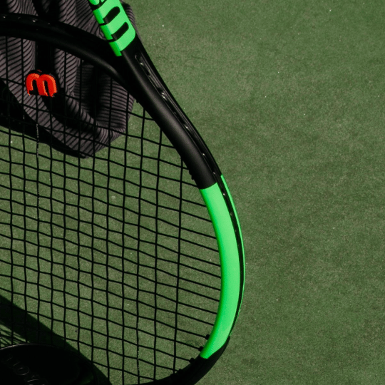 Three yellow Wilson US Open tennis balls rest on a black and blue tennis racket, all on a blue textured surface.